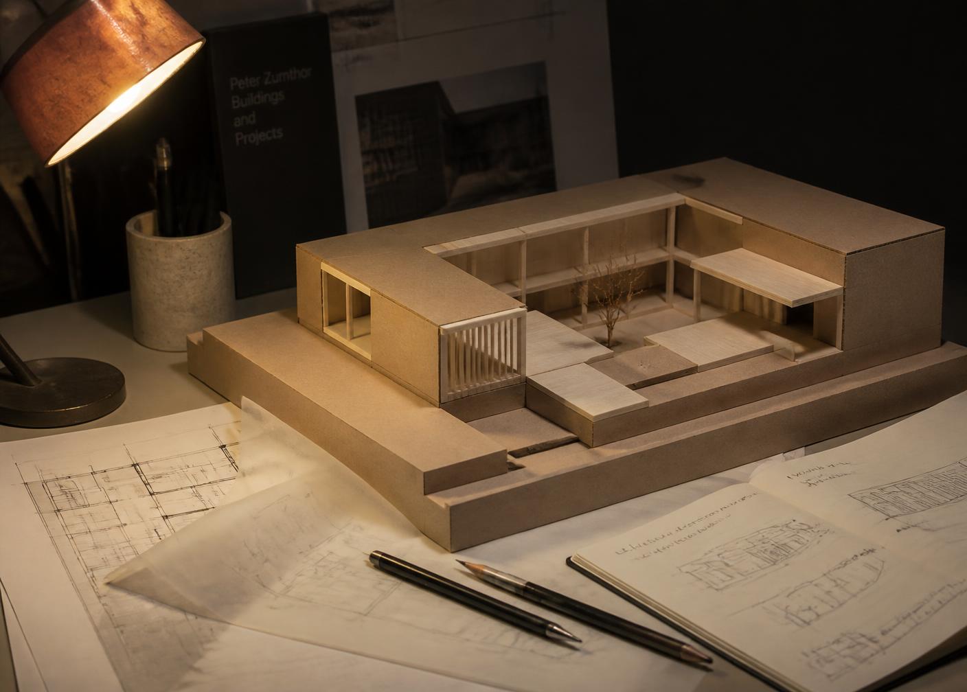 Chipboard and basswood massing model of a courtyard building beside plan drawings